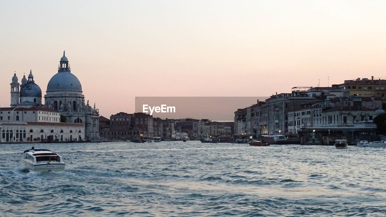 View of venetian canal against city and sunset sky