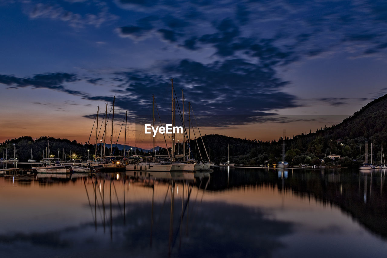 Sailboats moored at harbor against sky during sunset