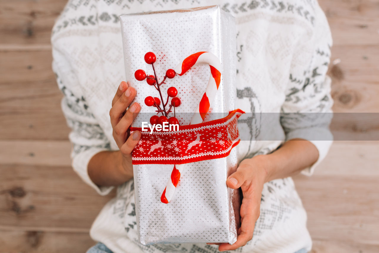 Midsection of woman holding christmas gift against wooden wall