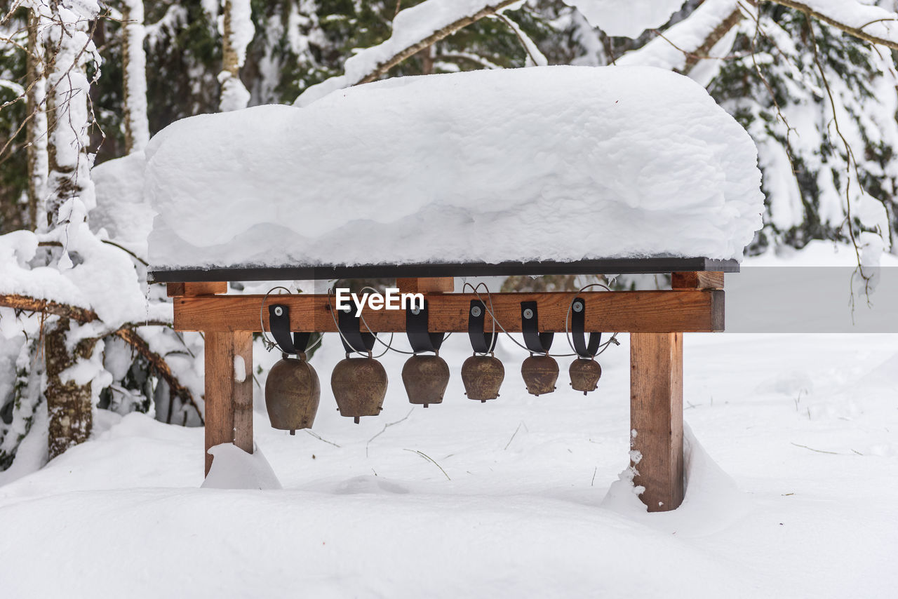 Old, metal alpine cow bells of various sizes hanging on a wooden structure. winter season trees path