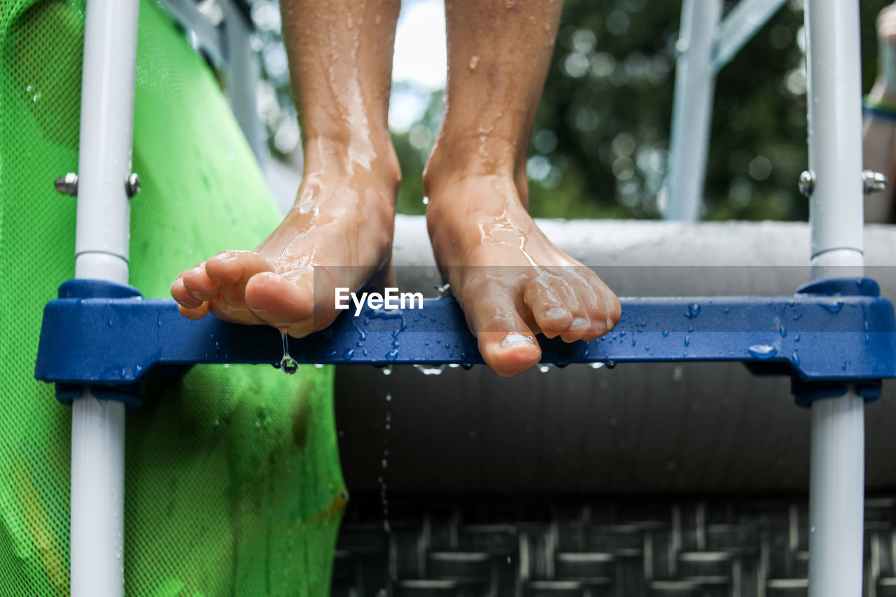 Close up of wet feet standing on pool ladder with water dripping off