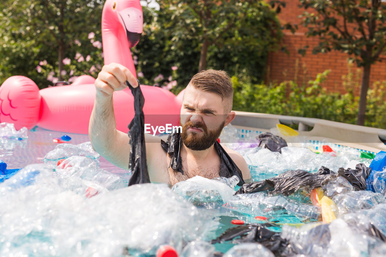 PORTRAIT OF YOUNG MAN HOLDING SWIMMING POOL IN WATER