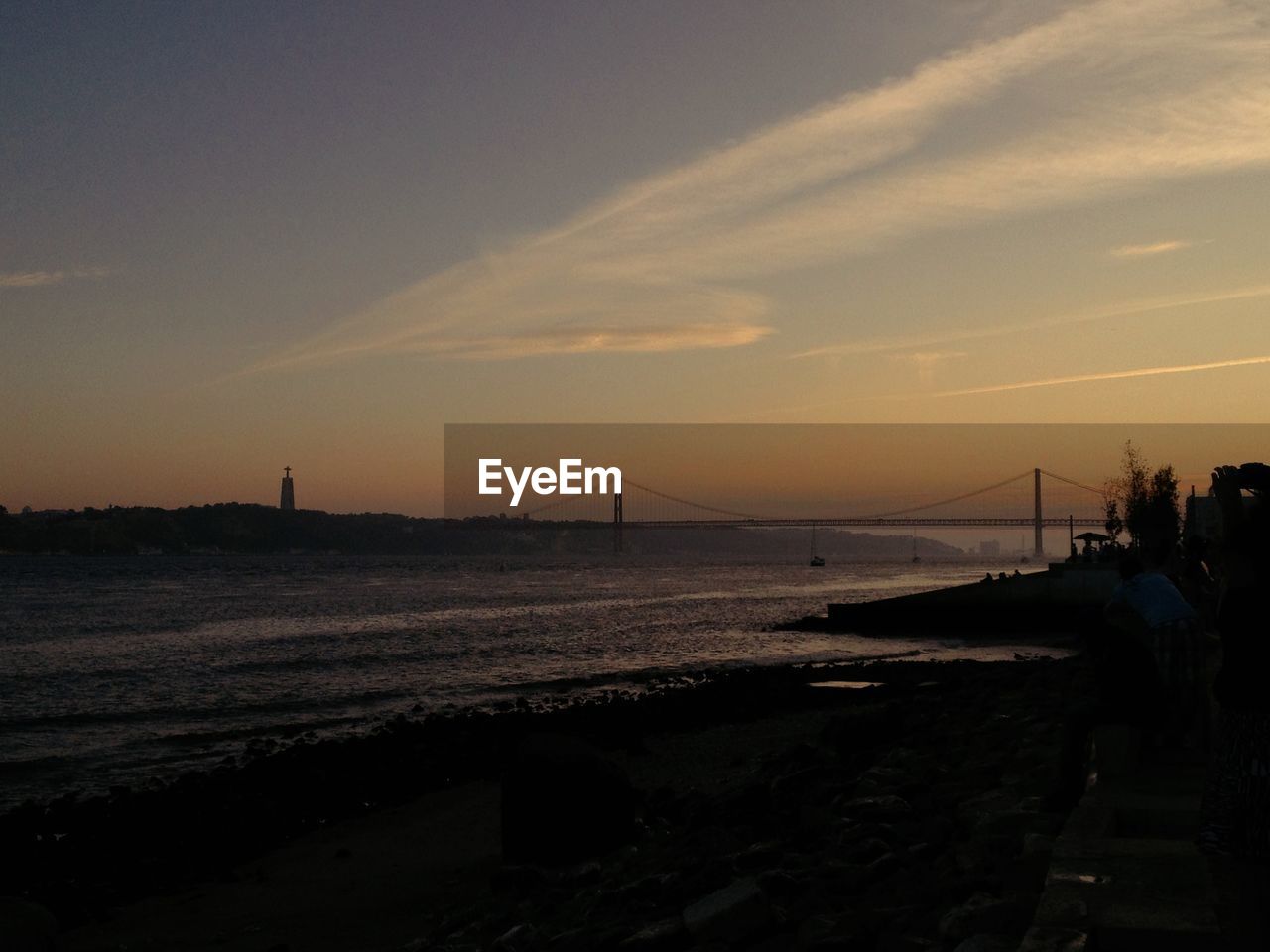 Distant view of 25 de abril bridge over tejo river against sky during sunset