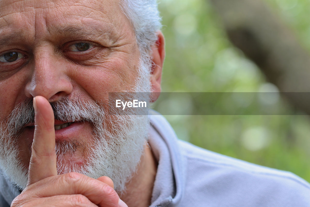 Close-up portrait of senior man with finger on lips