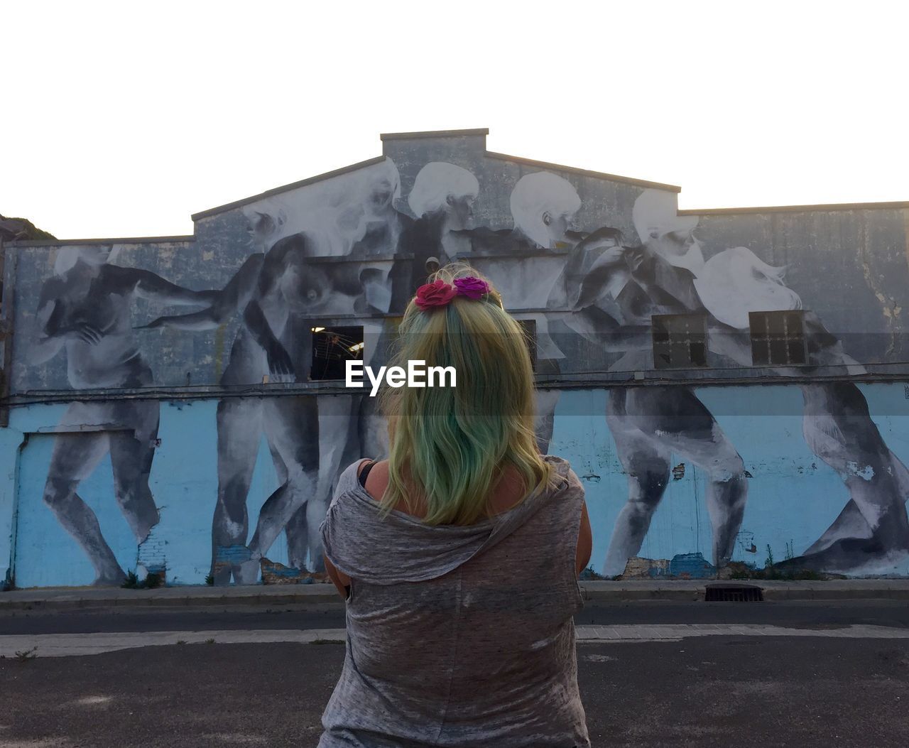 REAR VIEW OF WOMAN STANDING BY WALL