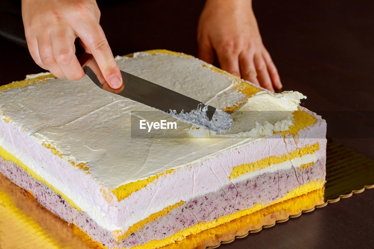 CLOSE-UP OF PERSON PREPARING CAKE ON TABLE