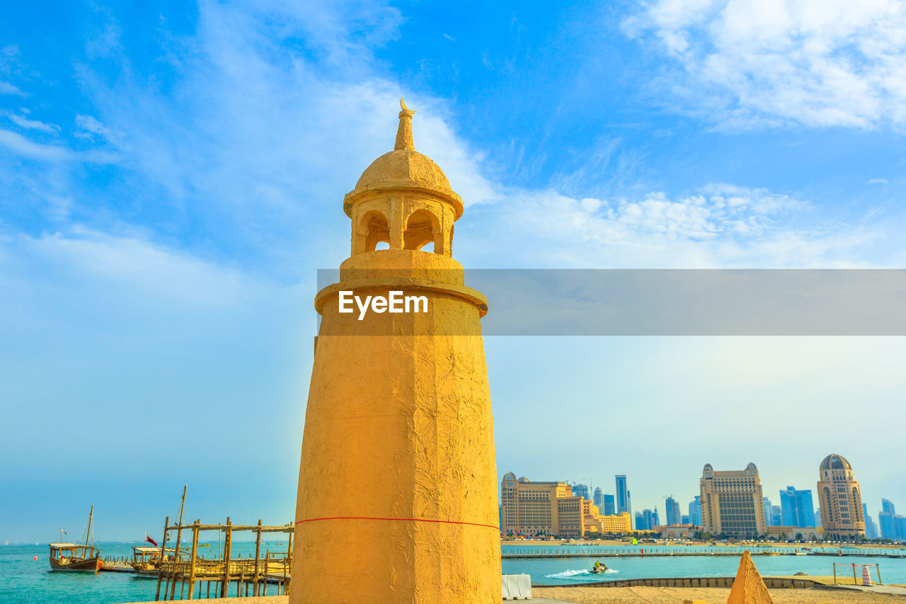 Lighthouse at beach in city against sky