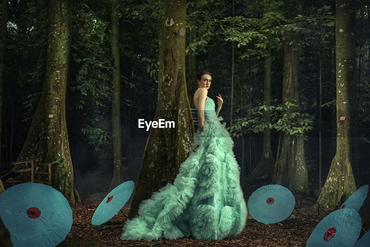 Woman standing by tree trunk in forest