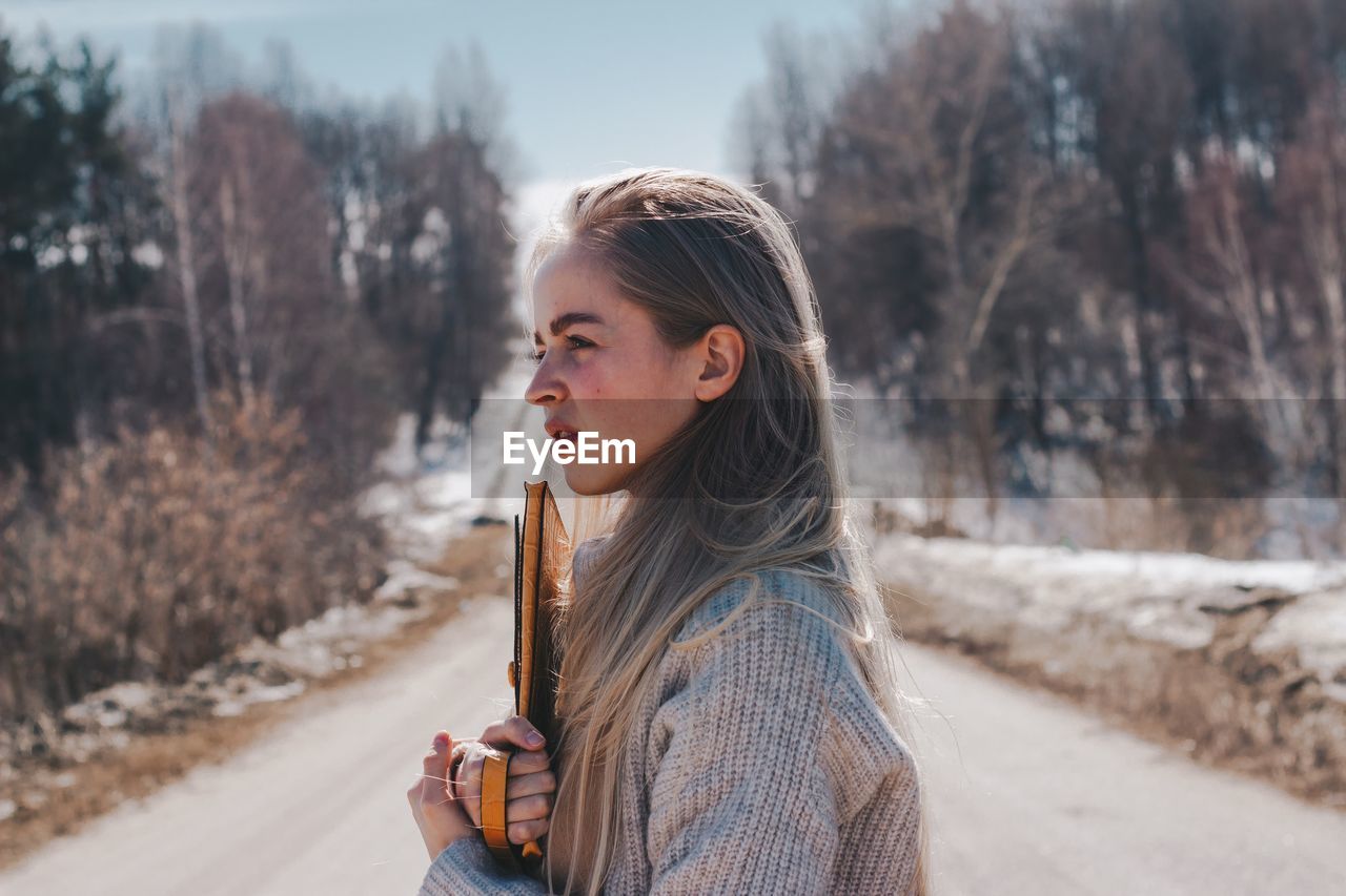 Side view of beautiful young woman looking away while standing in snow