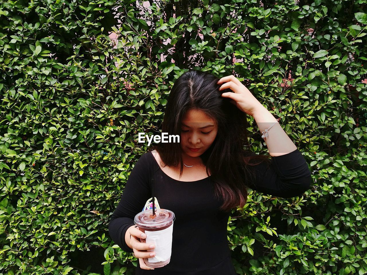 Young woman having drink while standing against plants