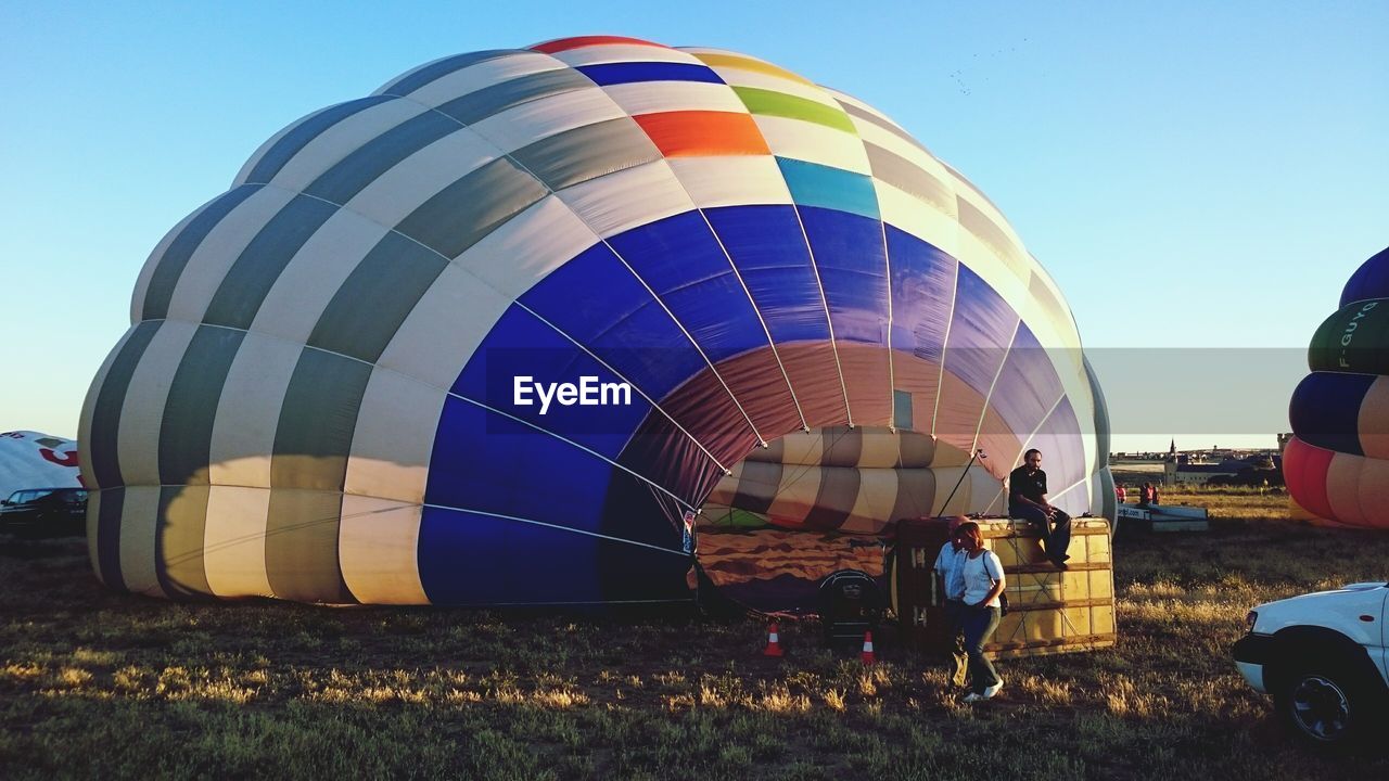 People walking by hot air balloon against clear sky