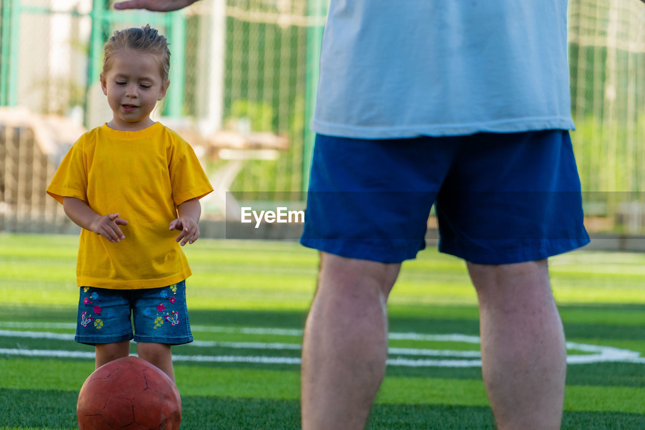 Cute little girl in yellow t-shirt going to kick the ball to father