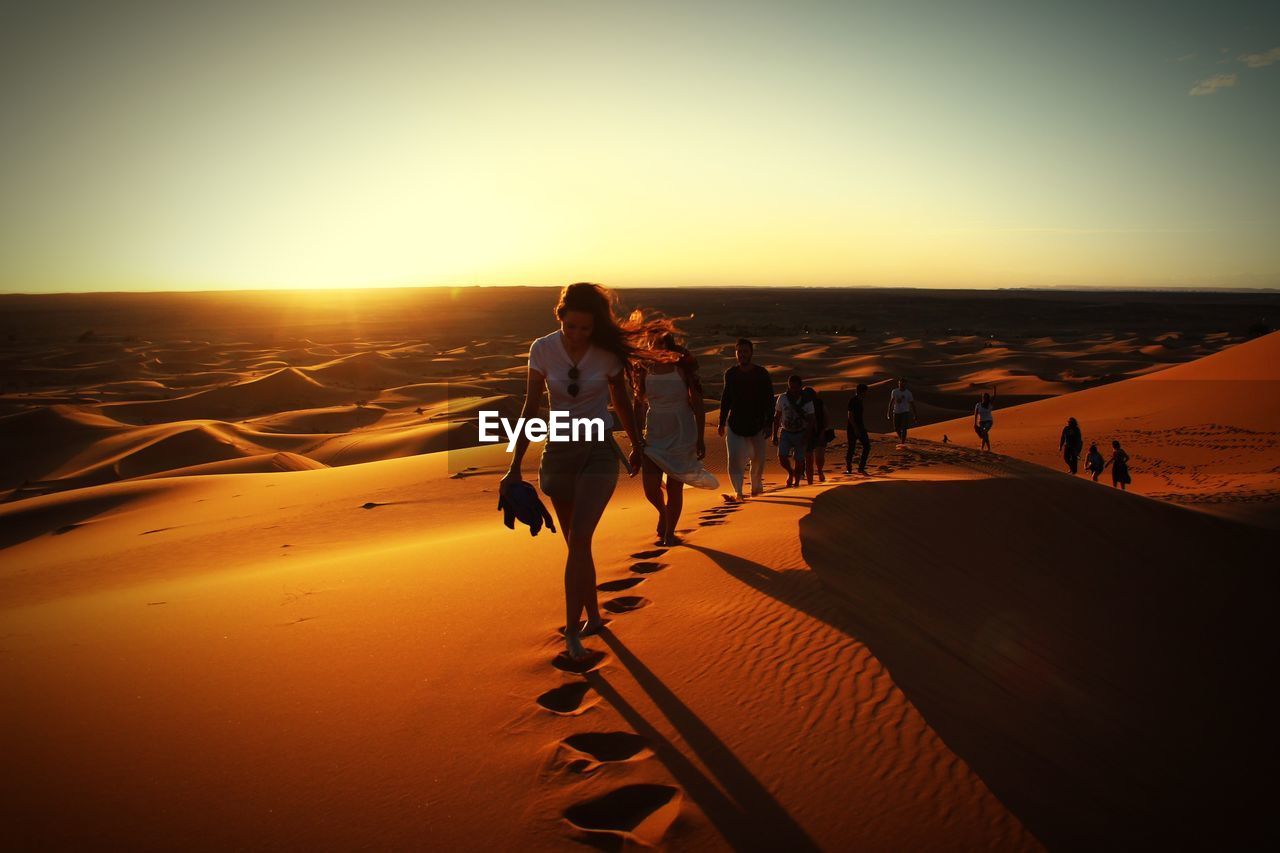 Full length of people walking on sand in desert during sunset