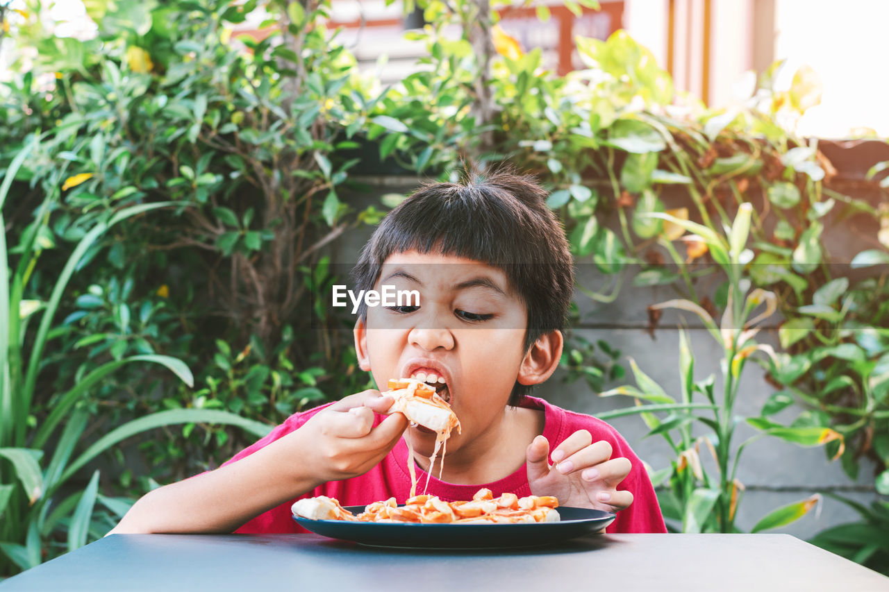 Asian cute boy in red shirt happily sitting eating pizza.