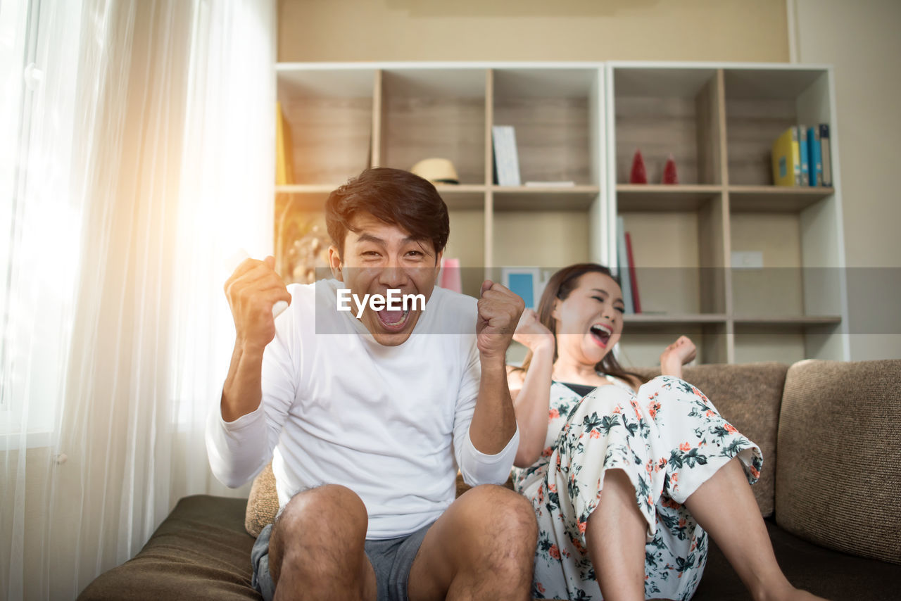 Happy couple clenching fists while watching tv on sofa at home