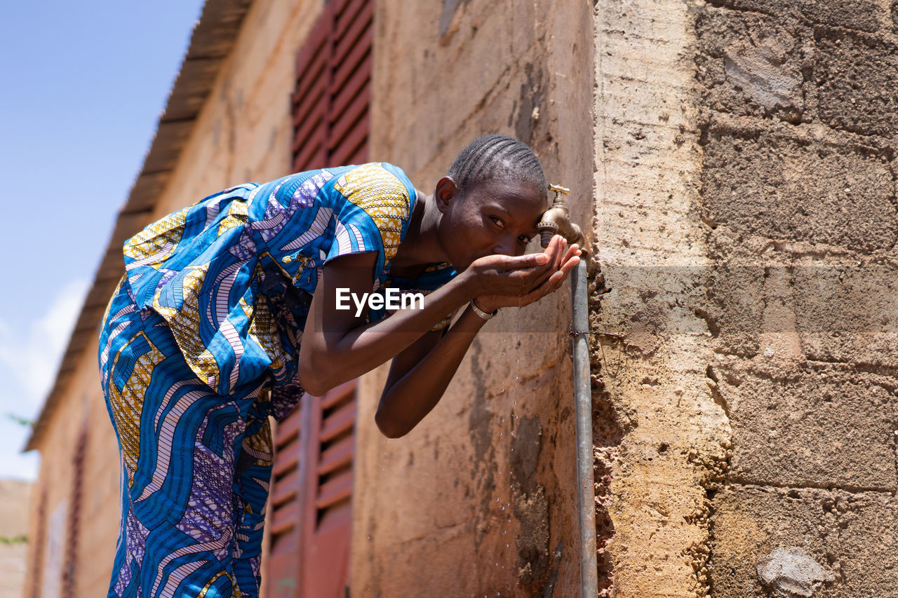 Girl drinking water from faucet against wall