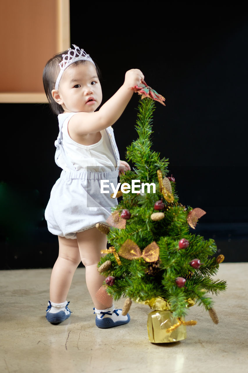 Full length portrait of cute baby girl standing by christmas tree at home