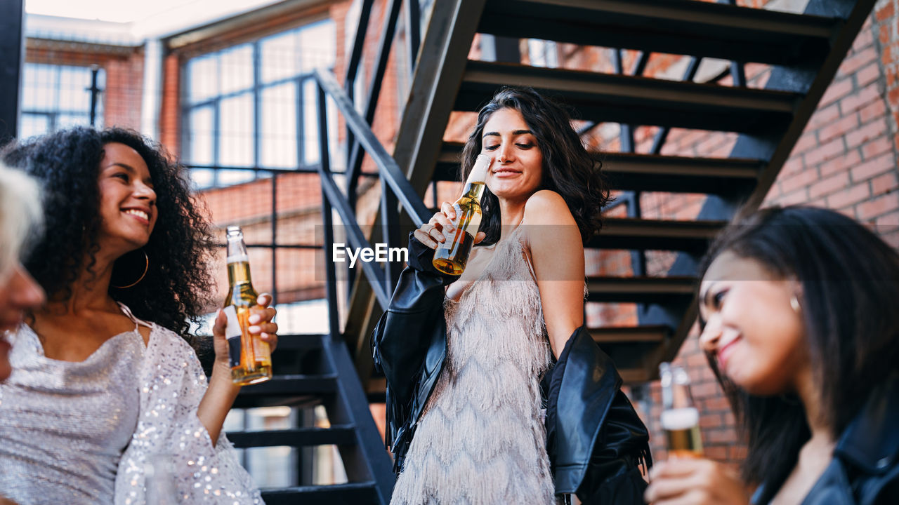 Happy friends holding beer bottle while standing outdoors