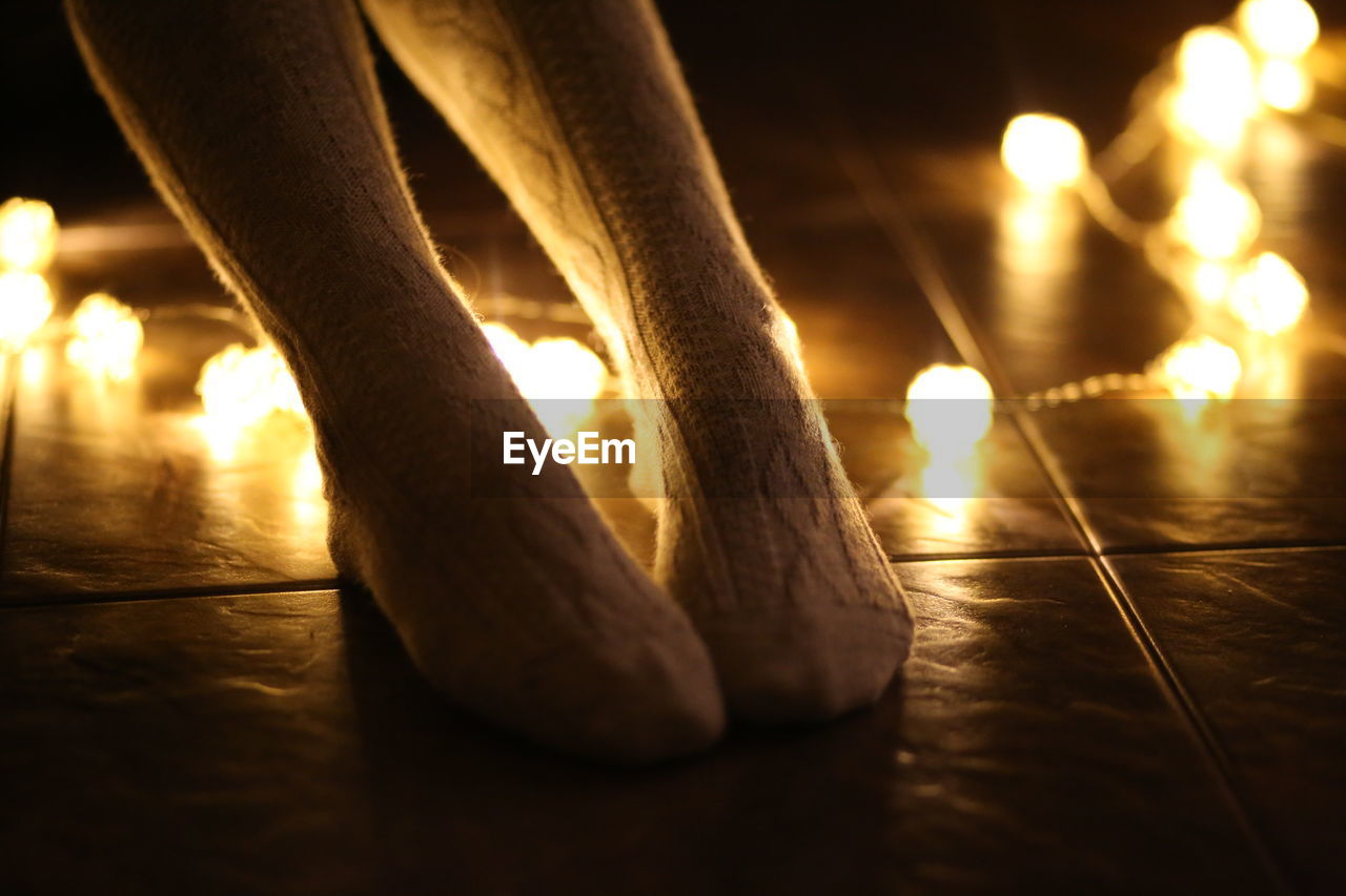 Low section of woman amidst illuminated string lights on tiled floor