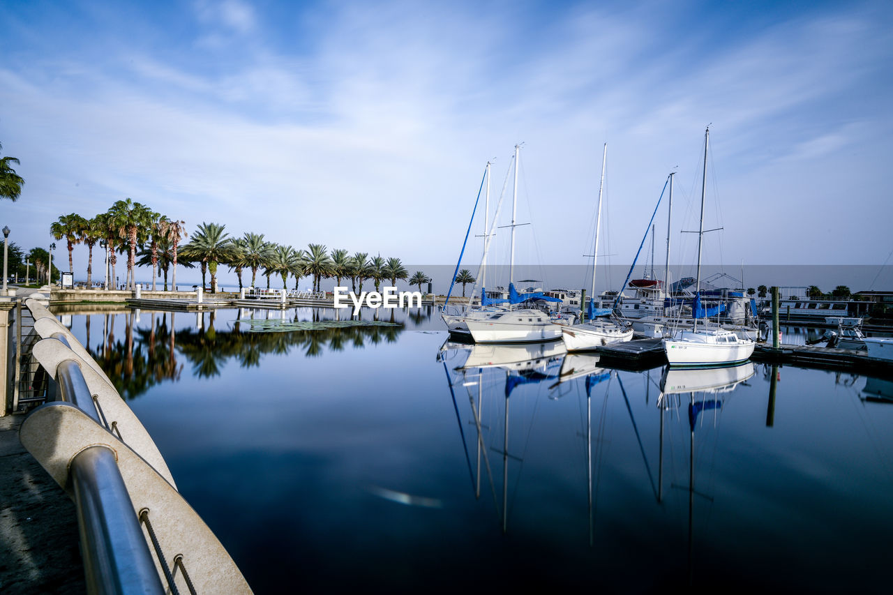 Sailboats moored on river against cloudy sky