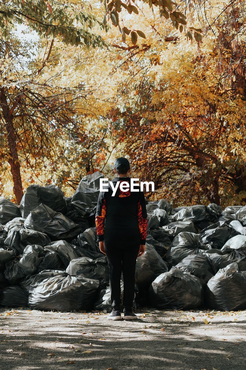 Rear view of man standing against garbage bags at park during autumn