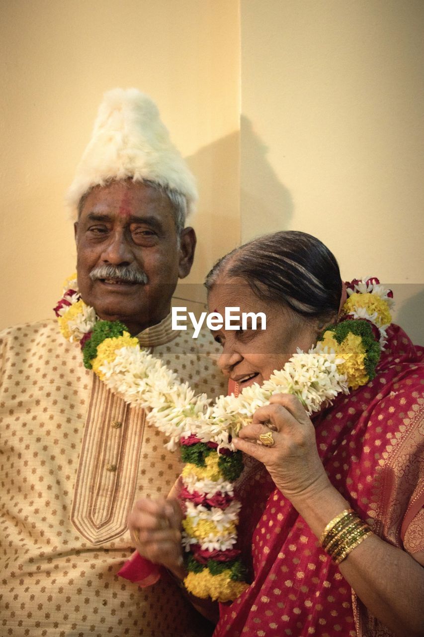 Senior couple wearing floral garland against wall