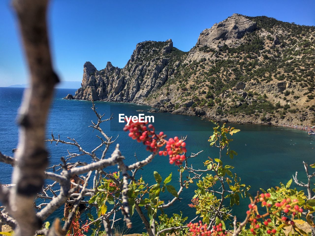 Scenic view of sea by mountain against blue sky