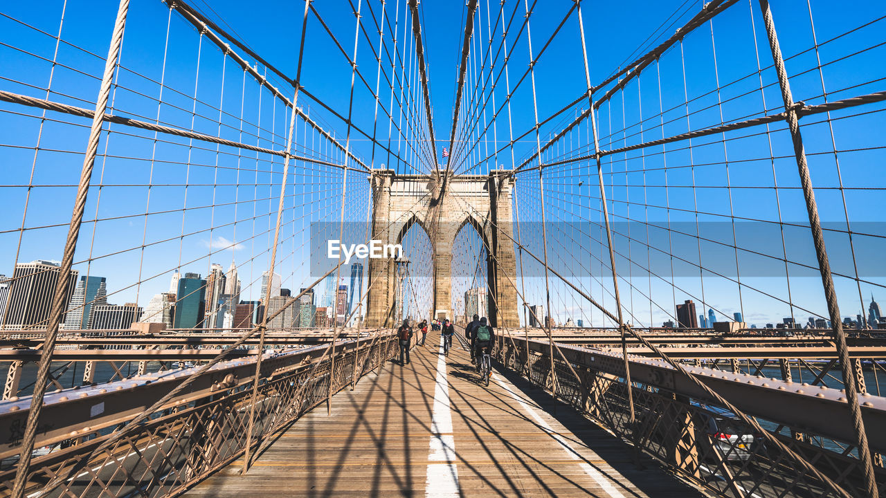 View of people on suspension bridge against blue sky