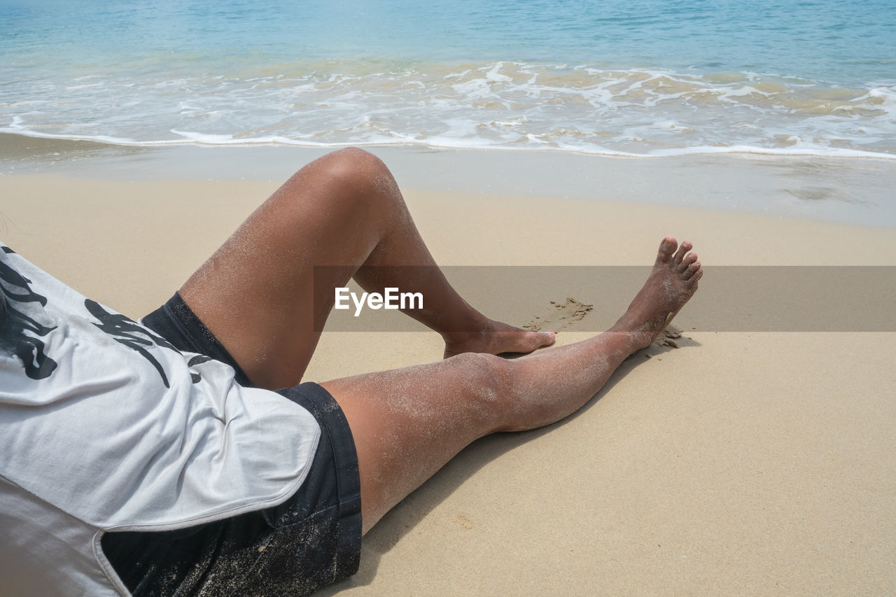 LOW SECTION OF MAN RELAXING ON SHORE