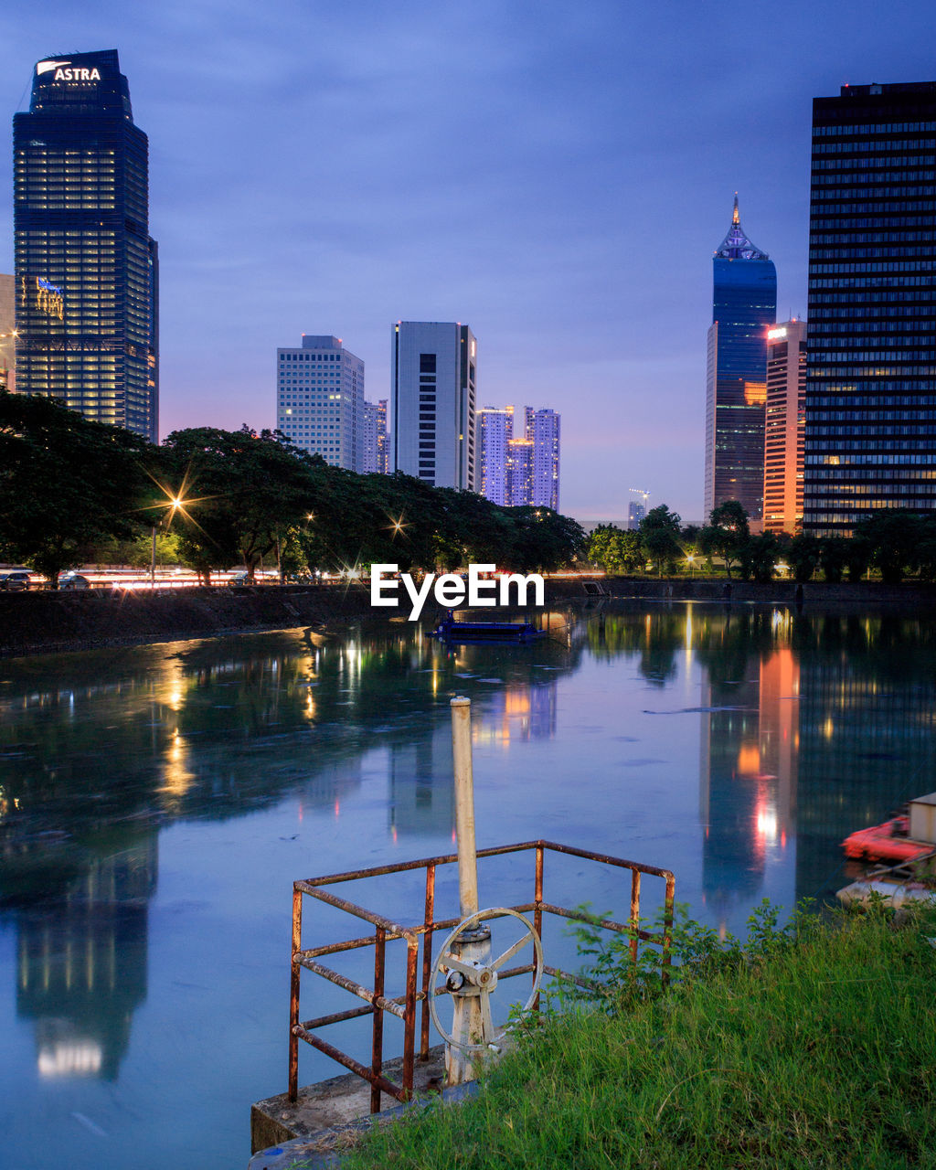 Illuminated buildings by river against sky in city