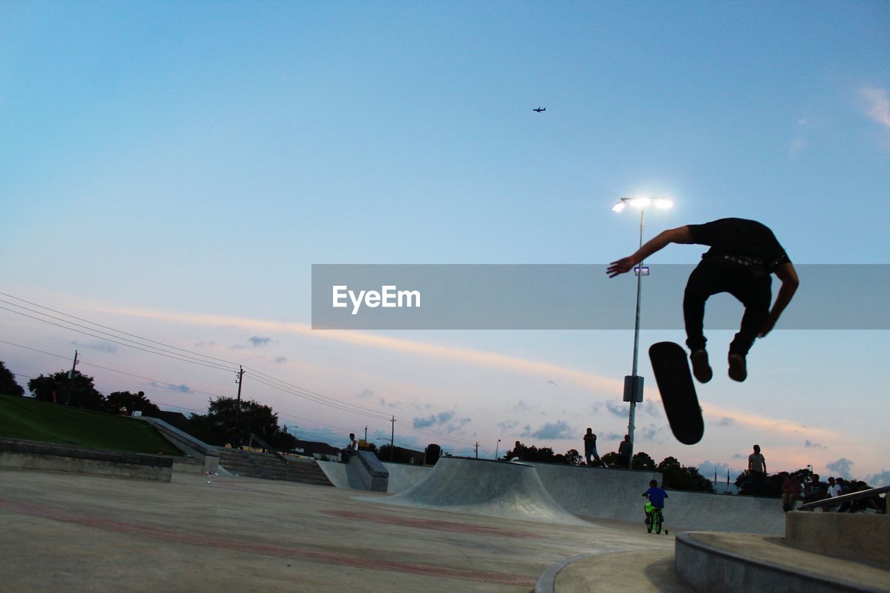 Man jumping while skateboarding against sky at park