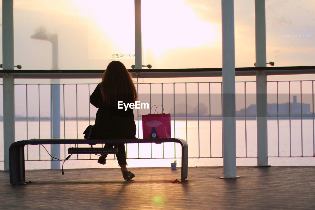 REAR VIEW OF WOMAN SITTING ON CHAIR IN GLASS WINDOW