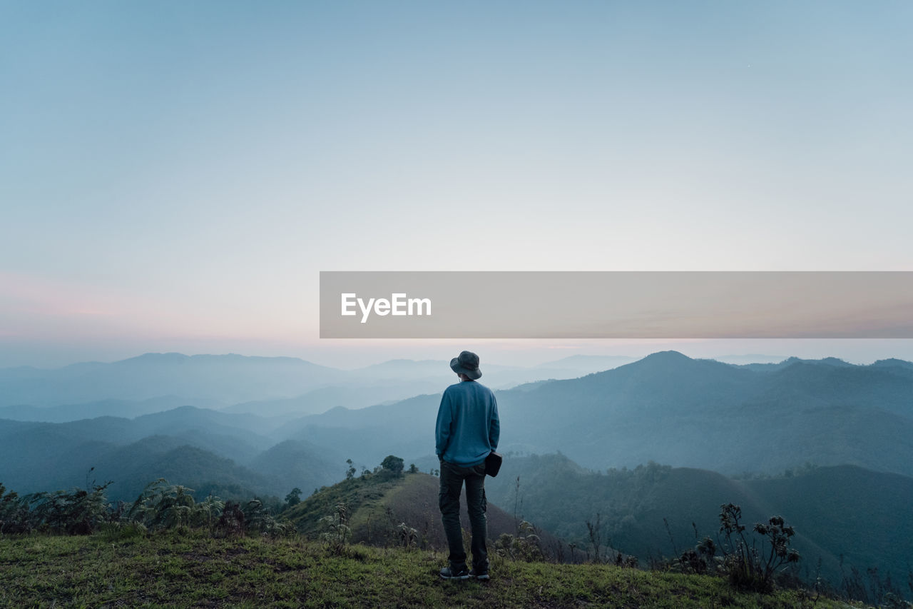 Rear view of man standing on mountain against sky