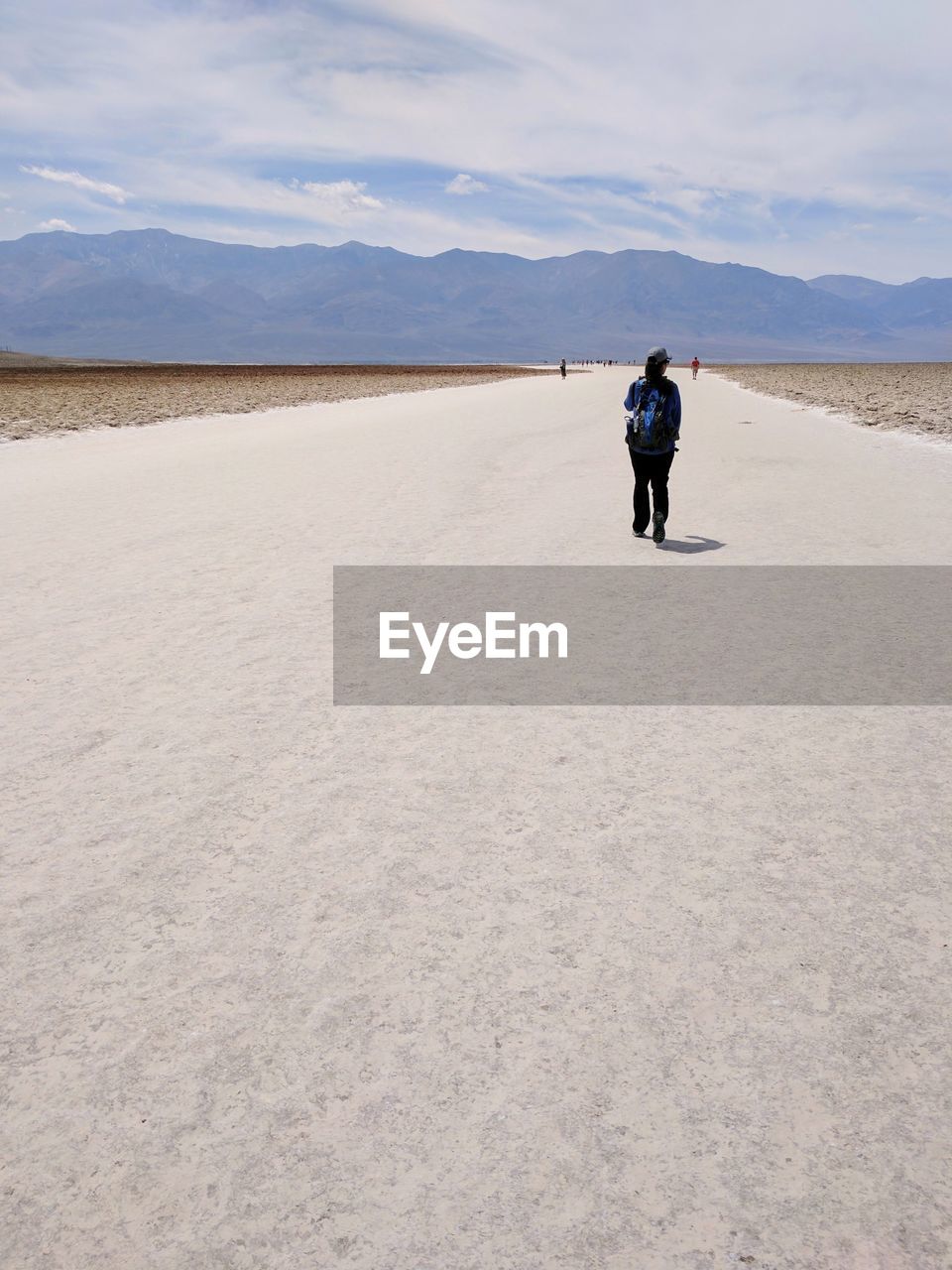 Rear view of woman standing on sand against cloudy sky