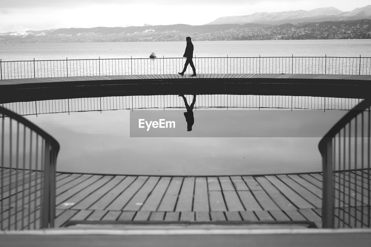 Silhouette man walking on pier by sea against sky