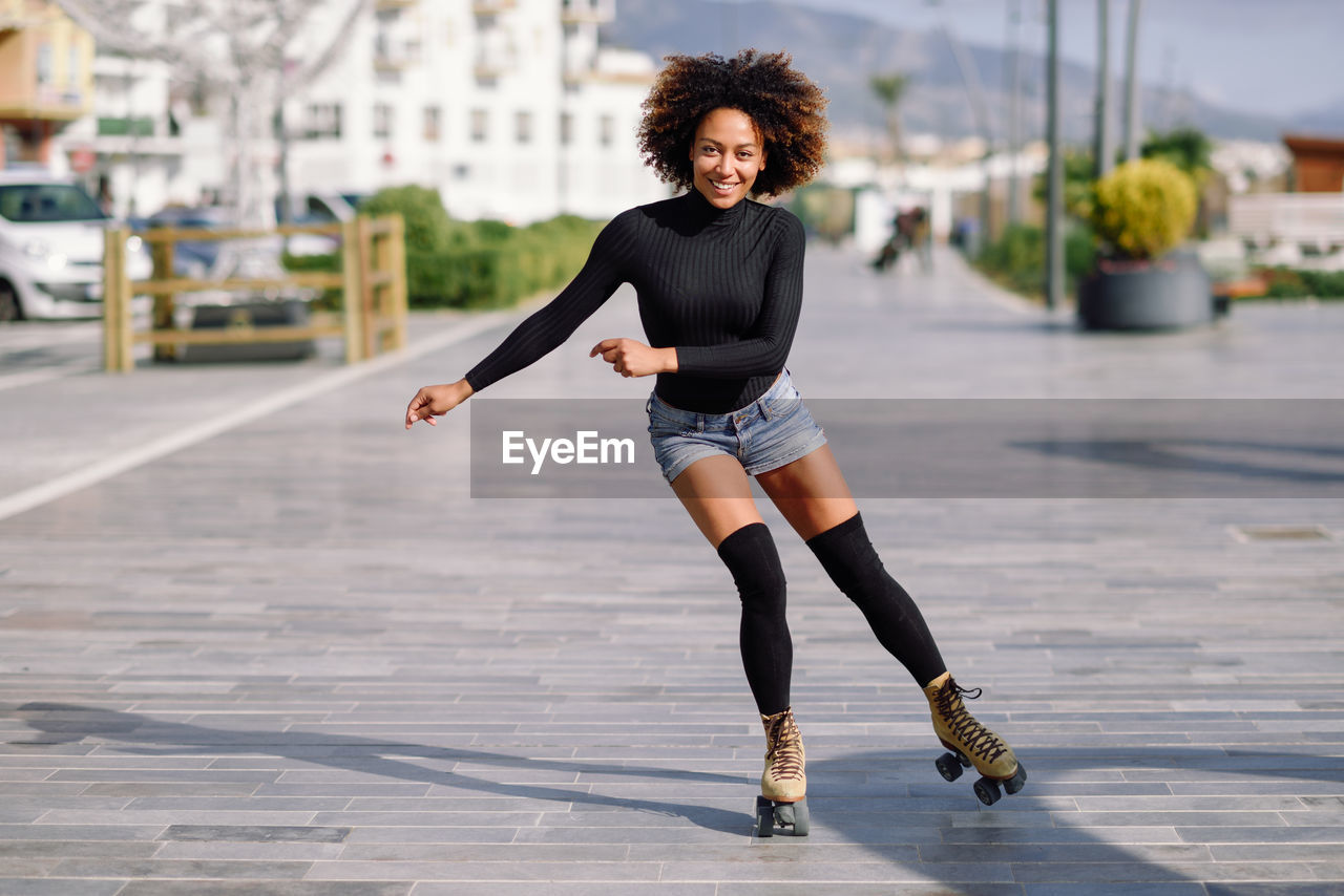 Portrait of woman roller skating on sidewalk in city