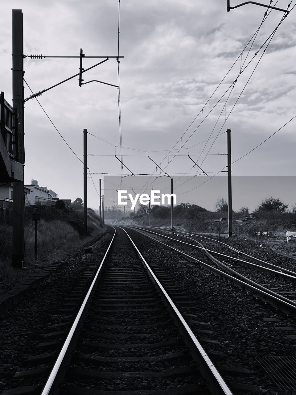 railroad track, track, line, rail transportation, cable, transportation, electricity, sky, transport, black and white, railway, power line, electricity pylon, technology, power supply, cloud, monochrome, nature, the way forward, no people, mode of transportation, monochrome photography, vanishing point, lane, diminishing perspective, overhead power line, architecture, wire, vehicle, outdoors, power generation, travel, public transportation, day, residential area, parallel, train station, tree, electrical network, sign, railroad station, electrical supply