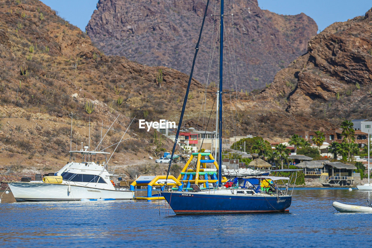 nautical vessel, water, transportation, mountain, mode of transportation, boat, vehicle, nature, sea, ship, bay, travel, land, day, travel destinations, no people, watercraft, scenics - nature, beauty in nature, rock, landscape, environment, sailboat, sky, outdoors, coast, mountain range, waterfront, boating, moored, beach, tourism, rock formation, mast, tranquility, architecture, harbor