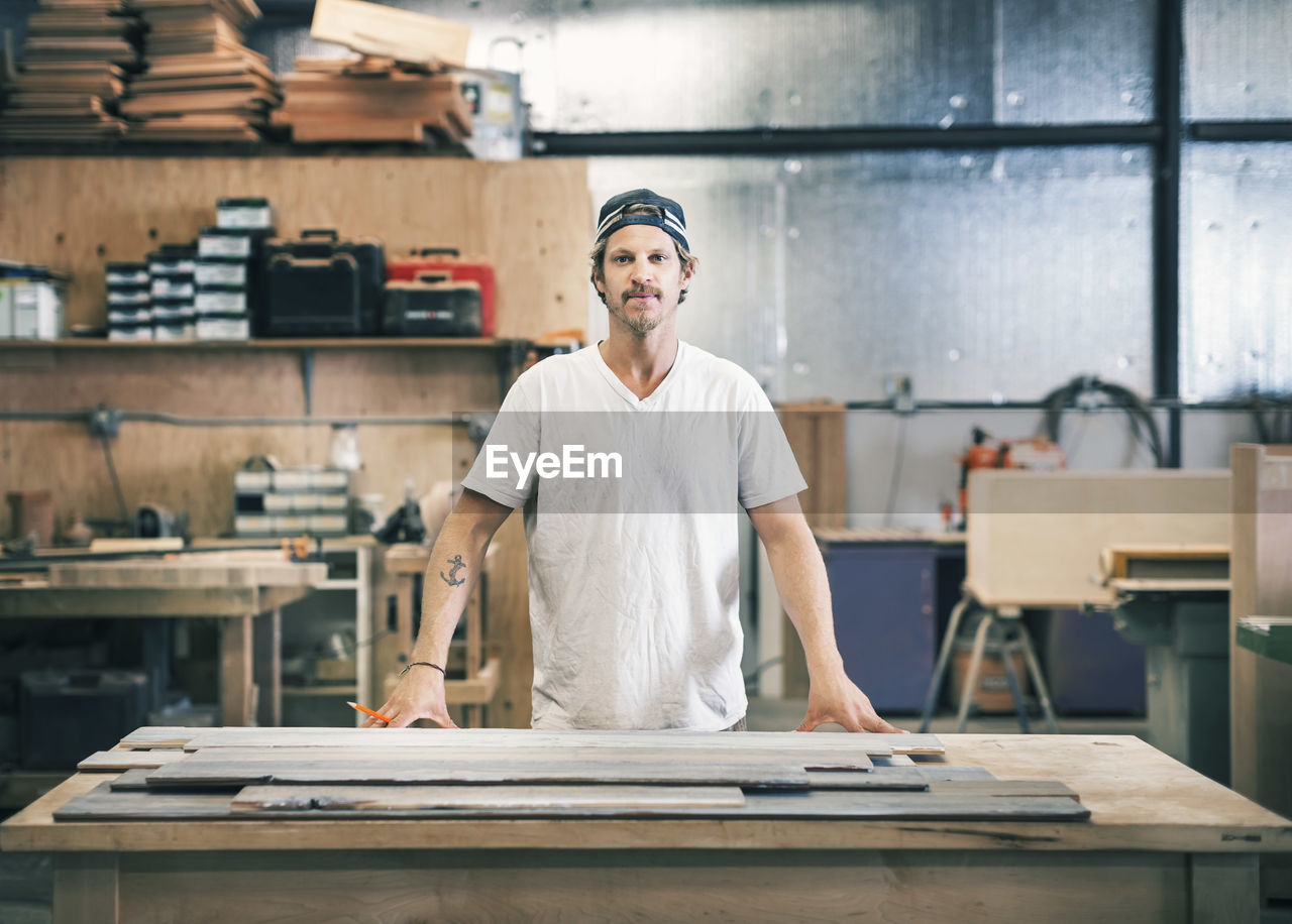Portrait of confident carpenter standing at workbench in workshop