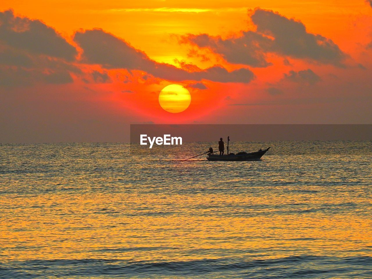 Silhouette people sailing on sea against orange sky