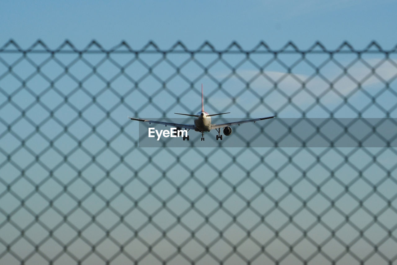 Close-up of airplane on chainlink fence against clear blue sky