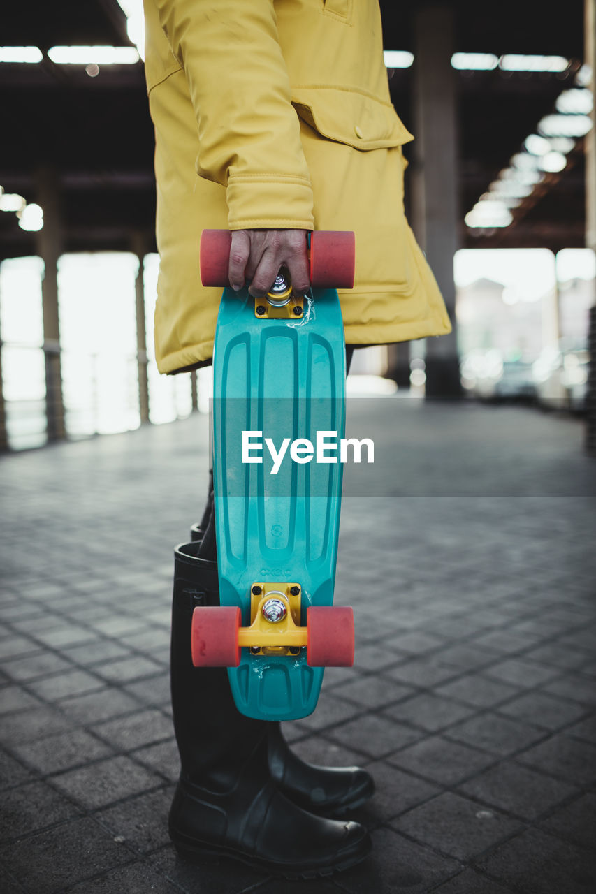 Young woman in yellow coat prepares and uses her electric skateboard.