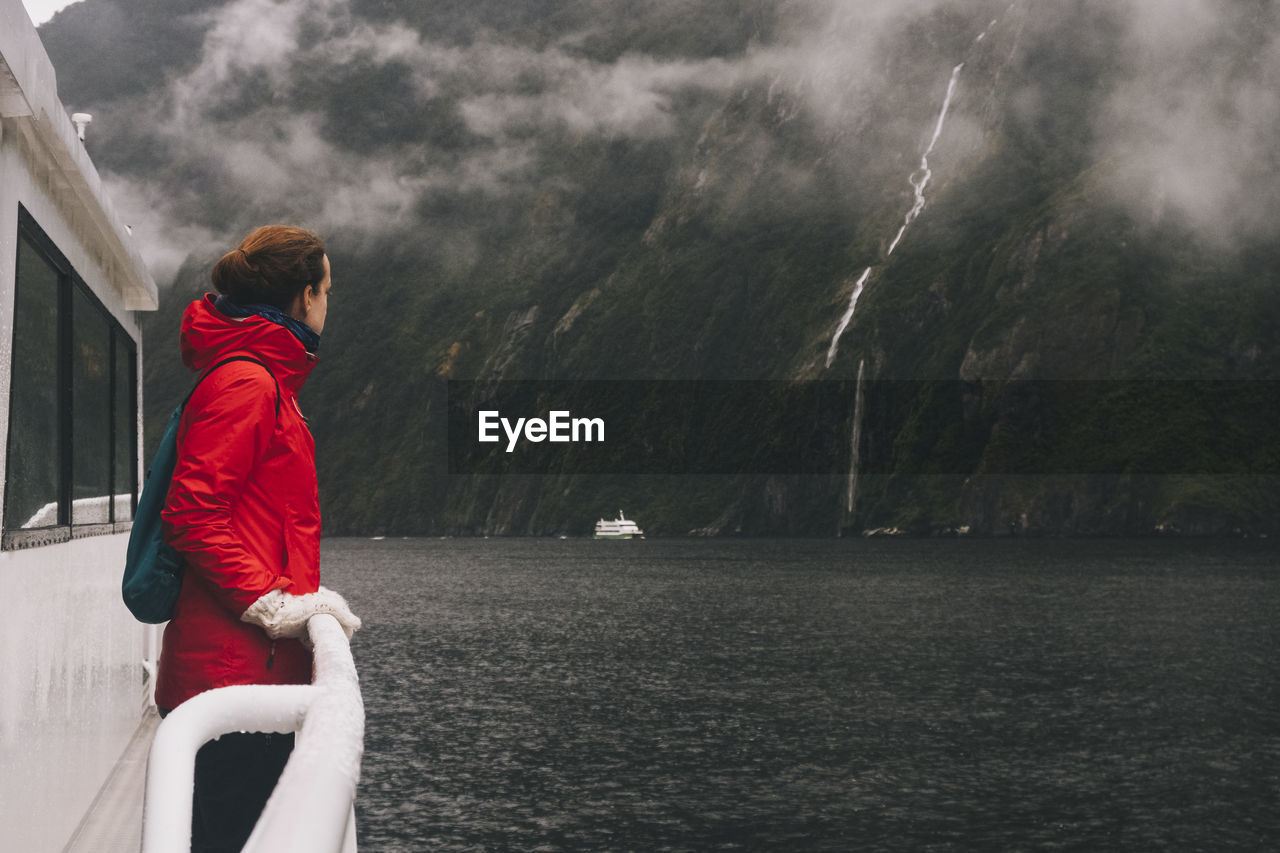 A woman stares up at the surrounding mountains in milford sound, nz