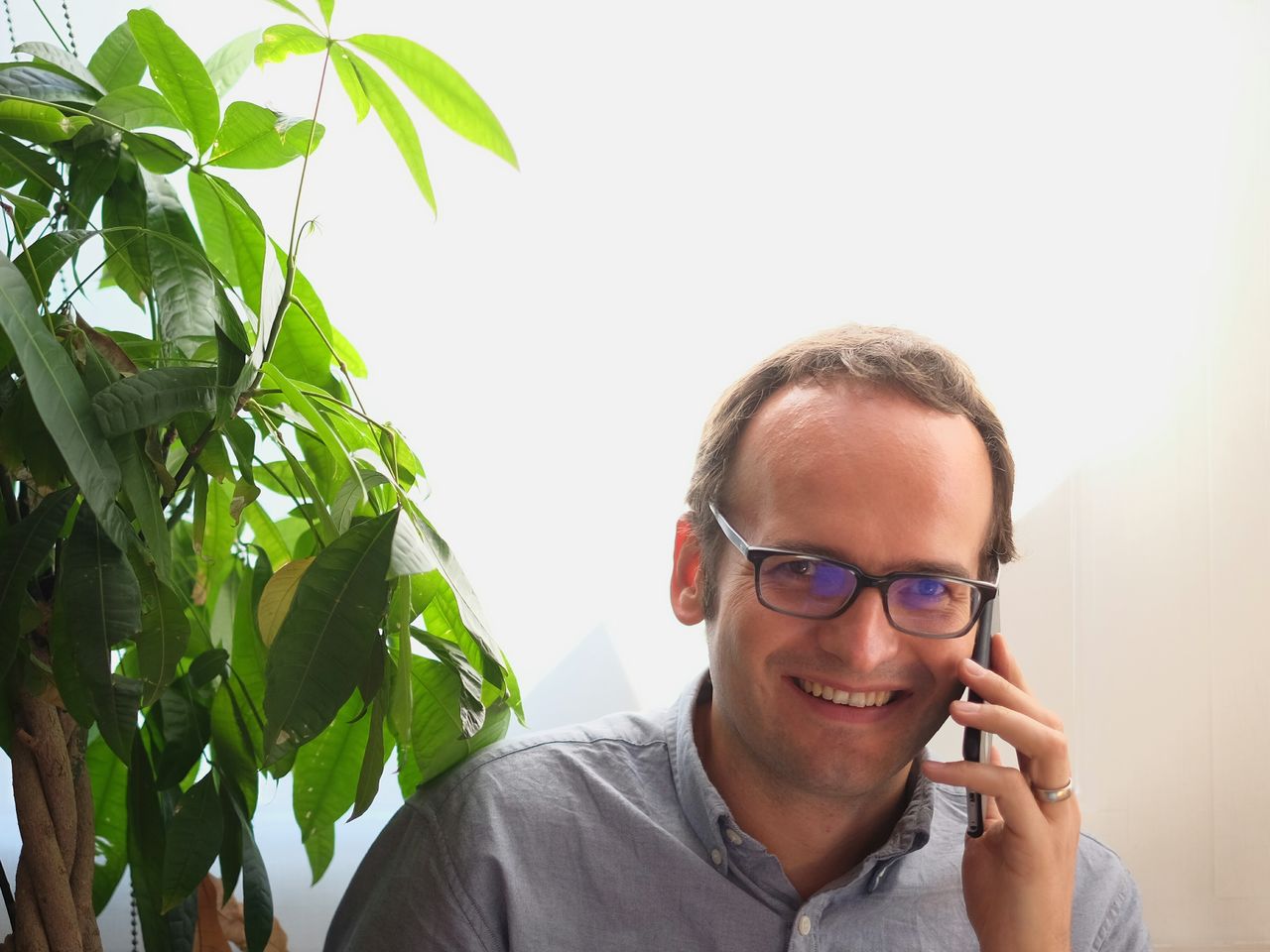 Portrait of happy man listening to mobile phone by plant against wall