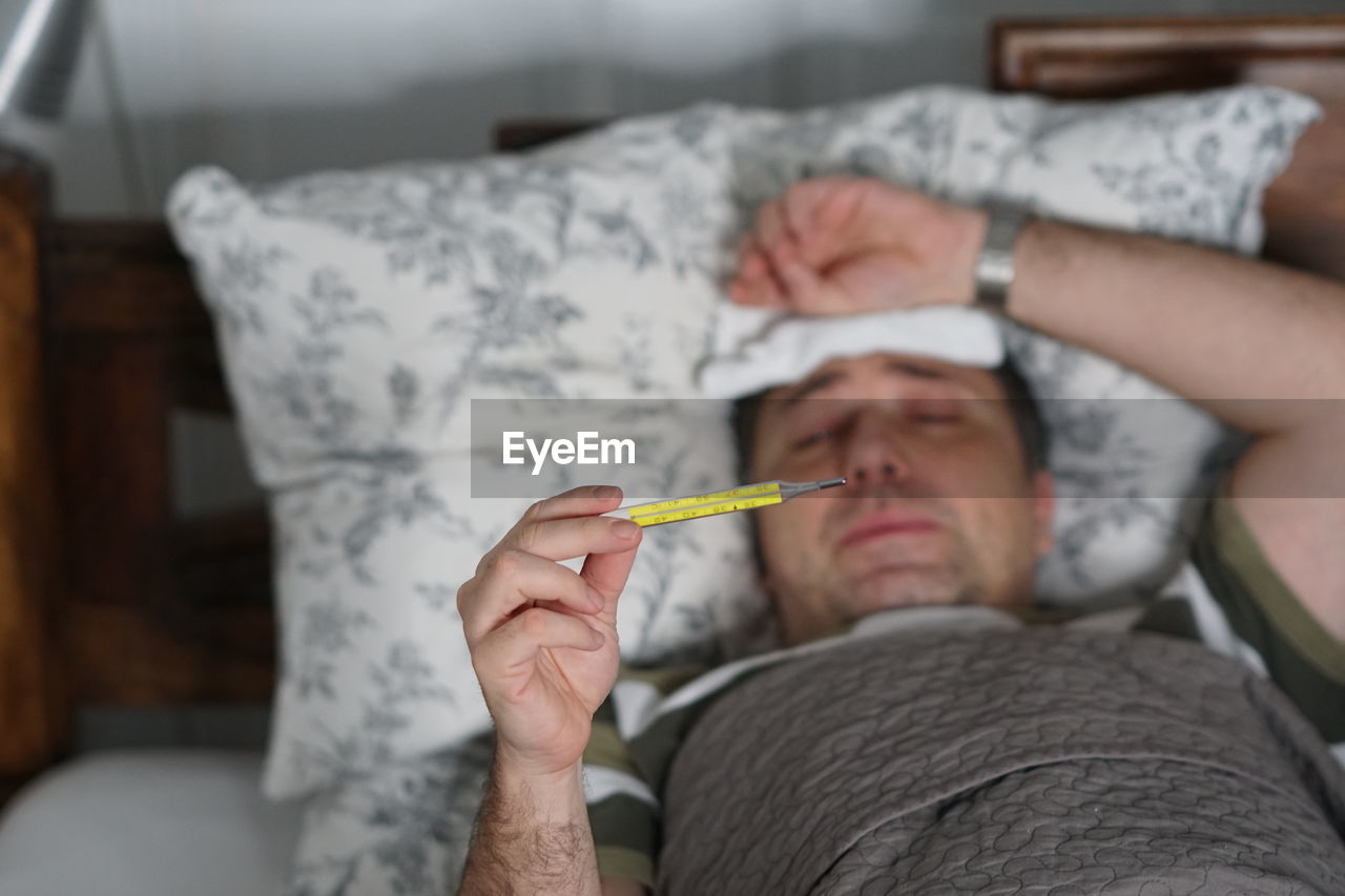 Man checking temperature while lying on bed at home