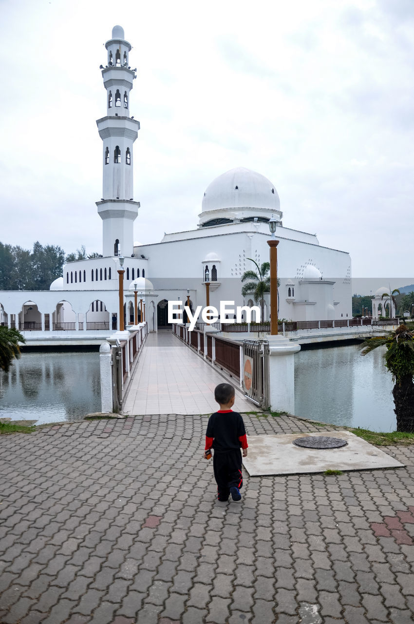 Rear view of boy walking towards floating mosque