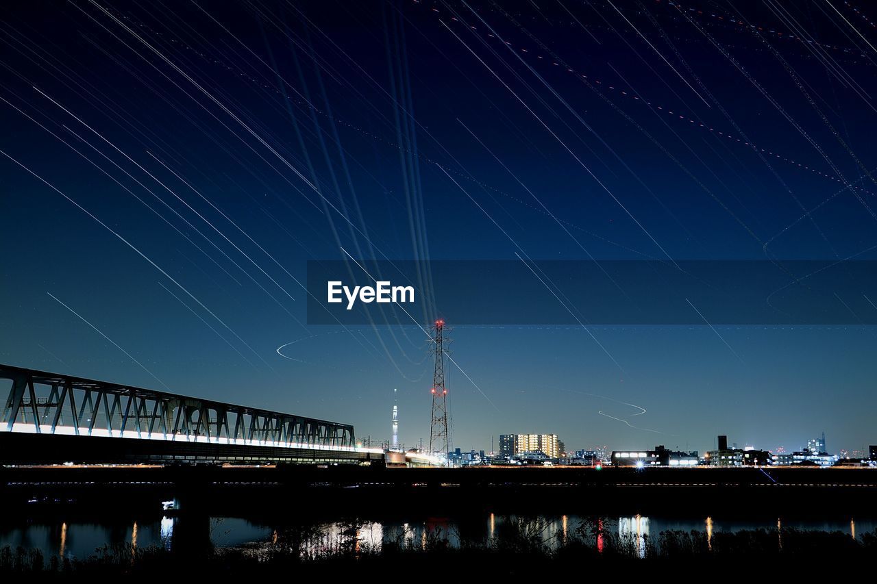 Low angle view of star trails over bridge at night