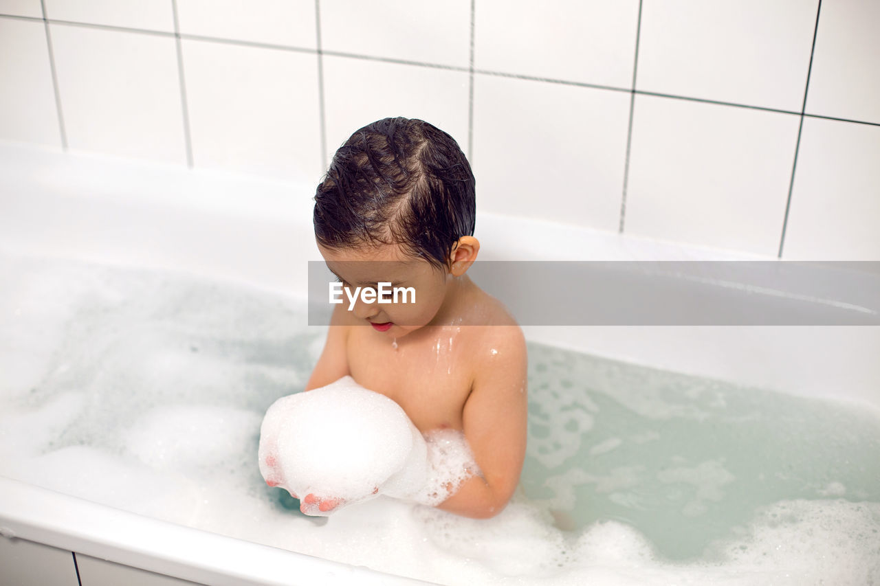 Boy with big eyes a caucasian child bathes in a white bath with foam