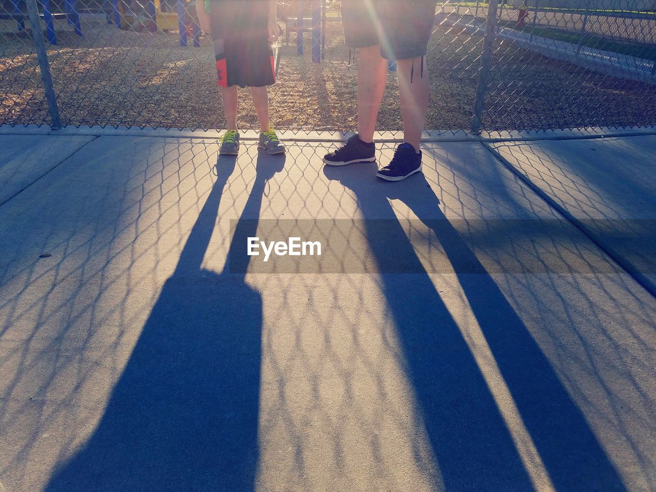 Low section of woman and boy standing by chainlink fence