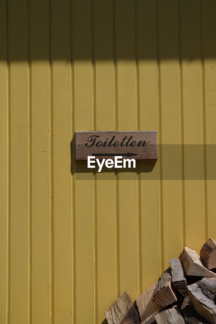 CLOSE-UP OF INFORMATION SIGN ON WOOD AGAINST WALL